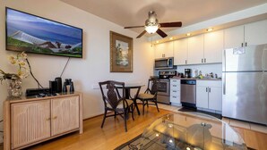 A modern kitchen with a flat-screen TV, a ceiling fan, and a dining area with a glass table.