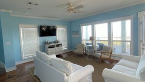 A living room with a white sofa, two armchairs, a ceiling fan, and a flat-screen TV mounted on the wall. - 2 Story Upscale Beachfront House With unobstructed Beach Views from every room. (Crystal Beach)