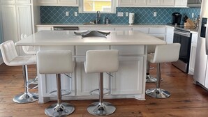 A modern kitchen with white cabinets, a central island with bar stools, pendant lighting, and a view of the outdoors through a window. - 2 Story Upscale Beachfront House With unobstructed Beach Views from every room. (Crystal Beach)