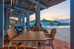 A covered outdoor seating area with a wooden table and chairs, overlooking a swimming pool and a residential building. - Great views, swimming pool, boardwalk to the beach, picnic tables, play area, co (Port Aransas)