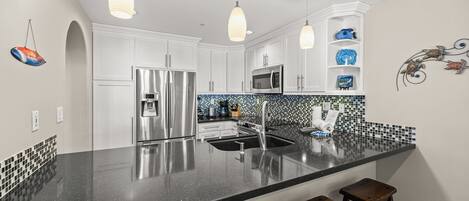 A modern kitchen with white cabinets, a black countertop, stainless steel appliances, and pendant lighting.
