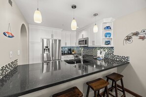 A modern kitchen with white cabinets, a black countertop, stainless steel appliances, and pendant lighting.