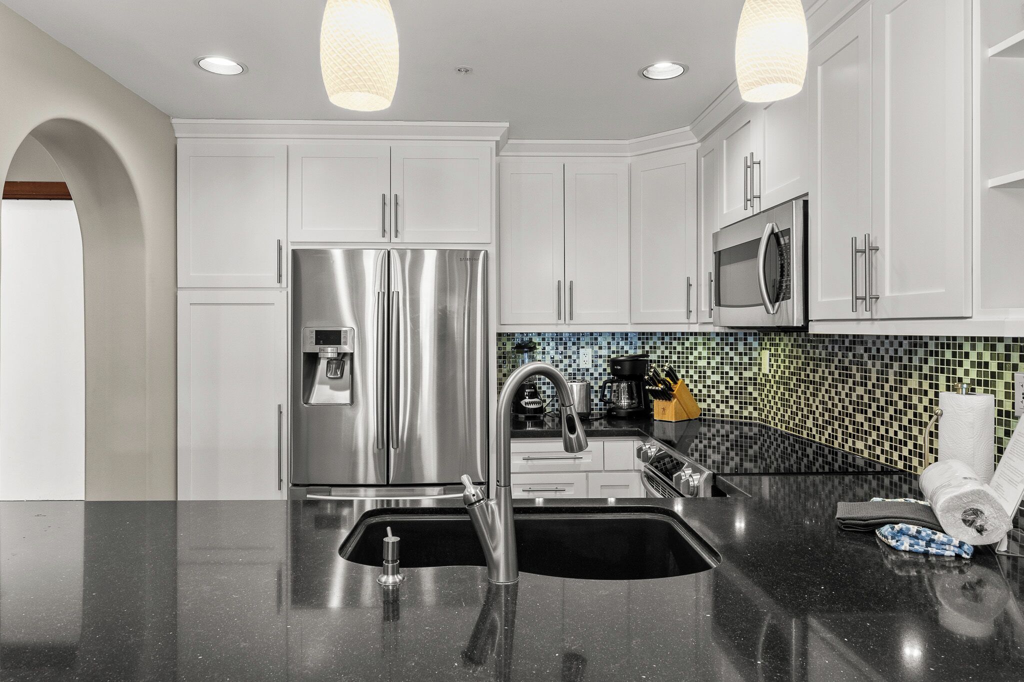 A modern kitchen with white cabinets, stainless steel appliances, a black countertop, and a tiled backsplash.
