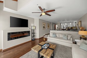 A modern living room with a flat-screen TV, a fireplace, a ceiling fan, a sofa, and a coffee table.