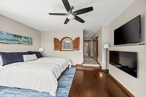 A bedroom with a bed, ceiling fan, TV, and artwork.