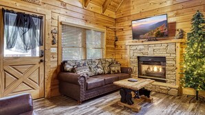 A cozy cabin interior with a stone fireplace, a wooden ceiling, a leather sofa, and a Christmas tree. - ER317 - The Cubby Hole - Great location - Close to town (Pigeon Forge)