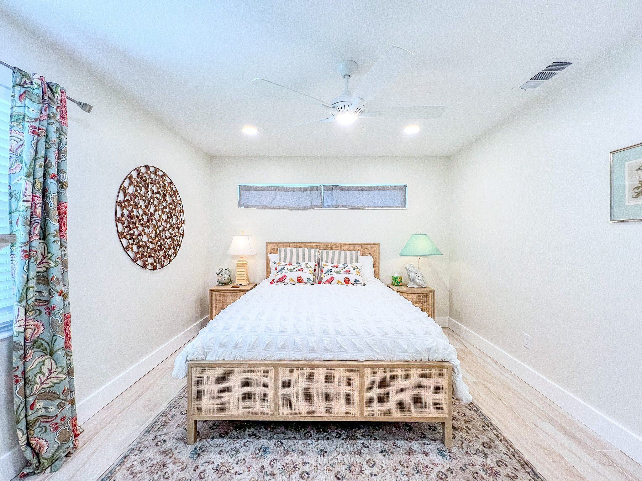 A bedroom with a bed, two bedside tables, a ceiling fan, a window, and a wall decoration.