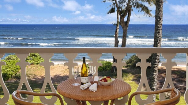 Un balcon avec une petite table en osier, mise pour deux personnes, une bouteille de vin et un panier de fruits.