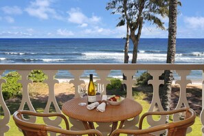 Un balcon avec une petite table en osier, mise pour deux personnes, une bouteille de vin et un panier de fruits.