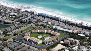 Luchtbeeld van een kustresort met een centraal gelegen zwembad, omringd door hotelgebouwen, een strand en een parkeerplaats.
