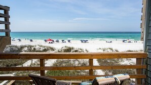 Uitzicht op het strand vanaf een houten terras, met strandparasols en ligstoelen.