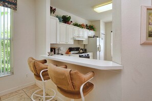 A kitchen with white cabinets, a white countertop, two brown bar stools, and a refrigerator. - 3BR Disney-Area Pool Home | 2 King Beds | BBQ Grill | Dog Friendly (Davenport)
