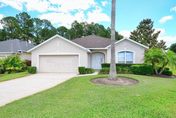 A single-story house with a garage, a well-maintained lawn, and a palm tree.