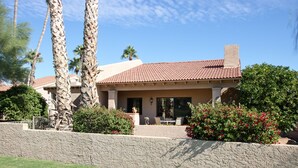 A two-story house with a tiled roof, a stone retaining wall, and a patio with outdoor furniture. - Rio Verde Townhouse overlooking the golf course. (Rio Verde)