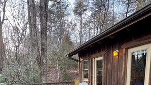 Une terrasse en bois avec des fauteuils à bascule et une table, donnant sur une zone boisée.