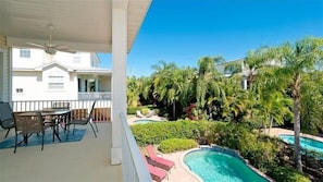 Área externa coberta com mesa e cadeiras, piscina e vista para um edifício branco e palmeiras.