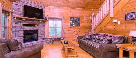 Ein gemütliches Blockhaus-Interieur mit Kamin aus Stein, Holzwänden, einer Couch und einer Uhr.