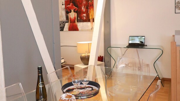 A modern dining area with a glass table, clear chairs, a laptop on a glass table, and a clock on the wall. - gluck duplex 97m2 city center 3br 2bth (Colmar)
