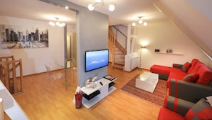A modern living room with a flat-screen TV, wooden flooring, a red sofa, and a staircase leading to an upper level. - gluck duplex 97m2 city center 3br 2bth (Colmar)