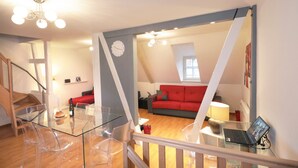 A modern living space with a glass dining table, clear plastic chairs, a red sofa, and a laptop on a small table. - gluck duplex 97m2 city center 3br 2bth (Colmar)