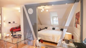 A modern bedroom with a bed, a laptop on a glass table, and a red sofa in the background. - gluck duplex 97m2 city center 3br 2bth (Colmar)