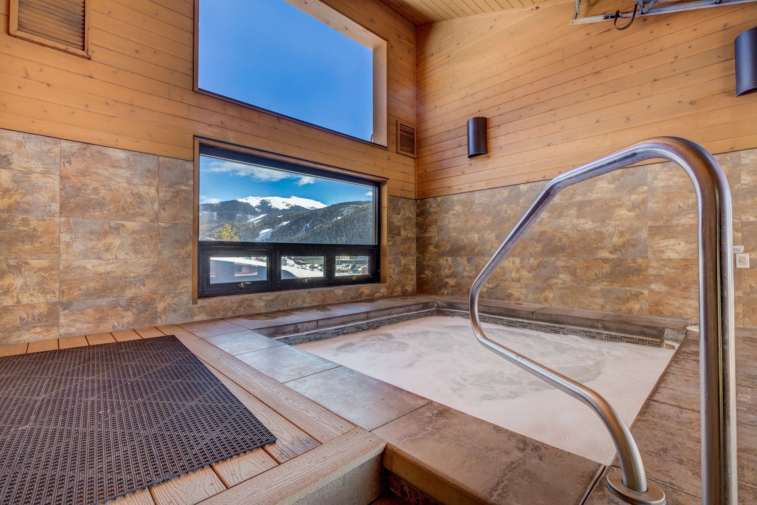A spa area with a stone floor, a wooden bench, a window with a mountain view, and a metal handrail.