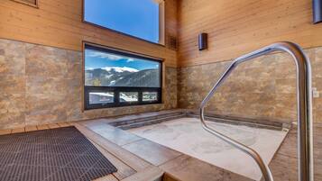 A spa area with a stone floor, a wooden bench, a window with a mountain view, and a metal handrail.