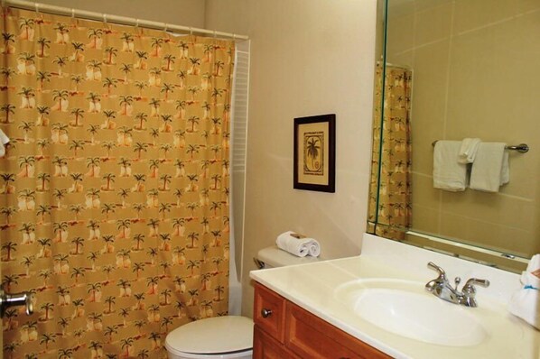 A bathroom with a toilet, a sink, a mirror, and a shower curtain with a palm tree pattern. - Mediterranea 210D-Steps to the private beach (Destin)