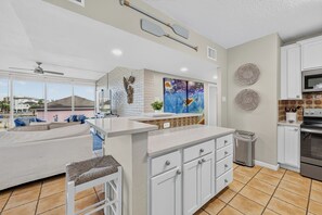 A modern kitchen with white cabinetry, a large island, and a view of the cityscape. - This spacious 2/2 is located right in the heart of Port A! Private fishing pier! (Port Aransas)
