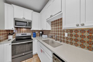 A kitchen with white cabinets, a microwave, a stove, a sink, and a coffee maker. - This spacious 2/2 is located right in the heart of Port A! Private fishing pier! (Port Aransas)