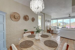 Un coin repas avec une table en bois, des chaises blanches et des sets de table en fibres tressées.