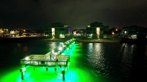 A waterfront property with a long dock extending into the water, illuminated by green lights.