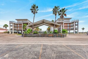 A multi-story hotel with a central atrium, palm trees, and a parking lot. - This spacious 2/2 is located right in the heart of Port A! Private fishing pier! (Port Aransas)