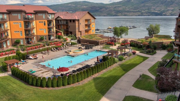 A hotel with a swimming pool, outdoor seating, and a view of a lake and mountains. - Barona Beach Lakefront Condo (West Kelowna)