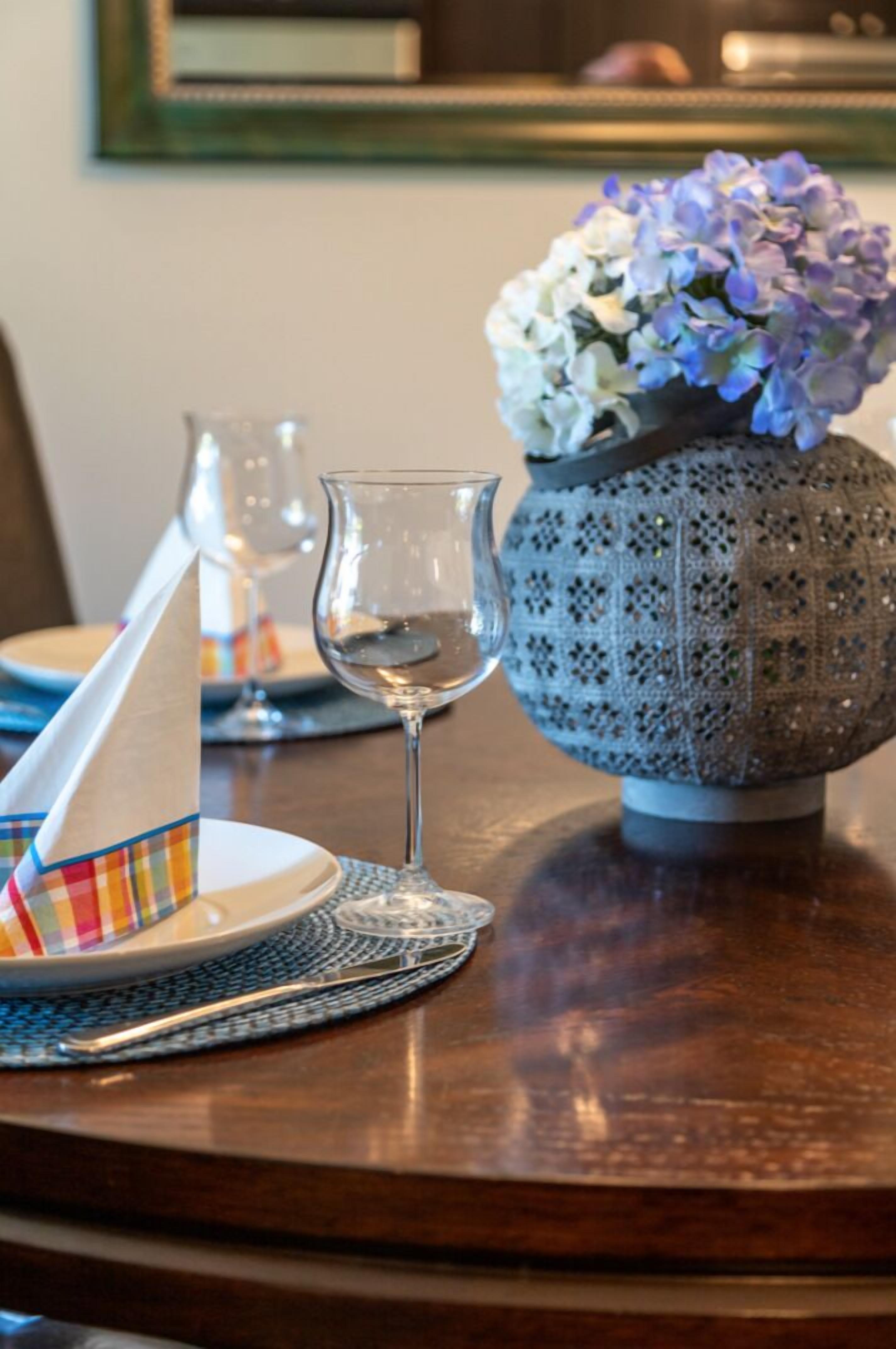 Una mesa de comedor con un florero, un vaso de agua y una servilleta colorida.