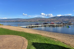 A lakeside view with a dock, boats, and mountains in the background.