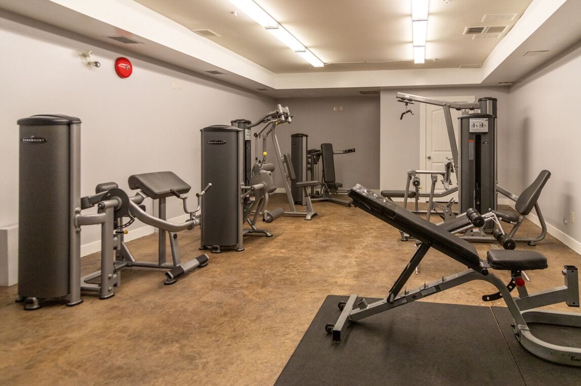 A gym with various exercise machines, a bench press, and a red fire alarm on the wall.