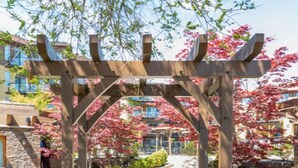 A wooden pergola structure in a garden with a pathway leading through it. - Barona Beach Lakefront Condo (West Kelowna)