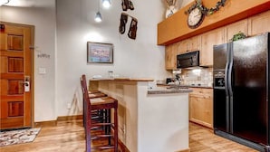 Une cuisine avec des meubles de rangement en bois, un réfrigérateur noir, un four à micro-ondes et un îlot central en bois doté de tabourets de bar.