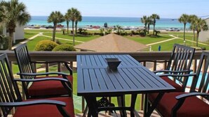 Un balcon avec une table et des chaises, donnant sur une plage bordée de palmiers et offrant une vue sur un ciel dégagé.