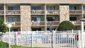 Un hôtel à plusieurs étages doté de balcons, d’une piscine et d’une clôture blanche en bois.