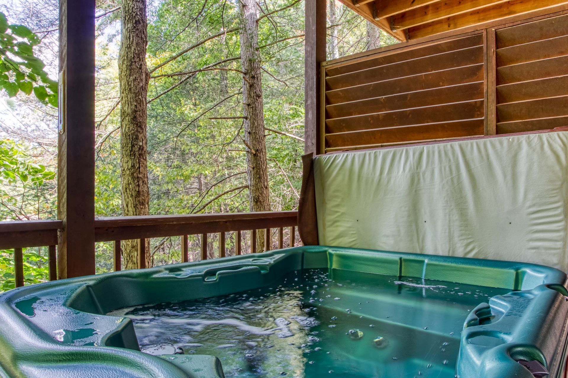 Un jacuzzi con vistas a un bosque desde una terraza de madera.