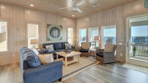 A spacious living room with a blue sofa, a coffee table, wicker chairs, and a ceiling fan. - Detail and craftsmanship are evident in every space. From the designer kitchen a (Port Aransas)