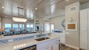 A modern kitchen with a large island, white cabinetry, and a view of the beach. - Detail and craftsmanship are evident in every space. From the designer kitchen a (Port Aransas)