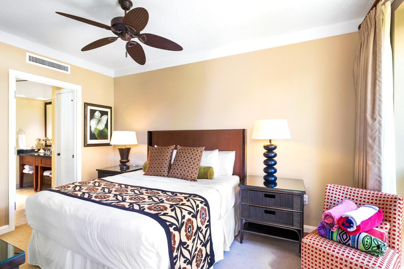 A hotel room with a bed, two bedside tables, a ceiling fan, a chair, and a window with curtains.