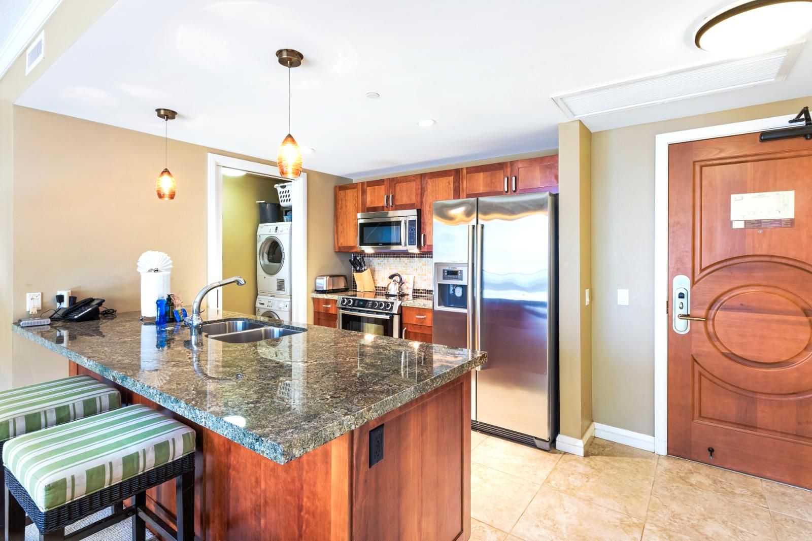 A kitchen with granite countertops, stainless steel appliances, wooden cabinets, and a large island with a sink.