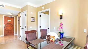 A dining area with a glass table, two chairs, a fan, and a vase with flowers.