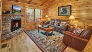 A cozy cabin interior with a stone fireplace, leather sofa, and a television mounted on the wall. - Dog Friendly! Hot Tub | Gameroom (Gatlinburg)