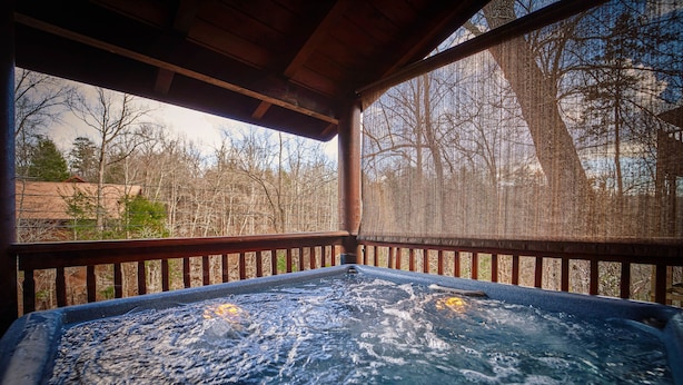 A hot tub with a wooden deck and a view of trees and a building in the background. - Dog Friendly! Hot Tub | Gameroom (Gatlinburg)