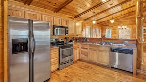 A modern kitchen with stainless steel appliances, wooden cabinets, and a wooden floor. - Dog Friendly! Hot Tub | Gameroom (Gatlinburg)